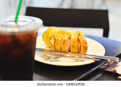 Blurry Iced Black Cold Brew Coffee In Plastic Glass Grab Focused At Bakery (sausage Pie) In White Plate With Cutlery On Dark Wooden Table, Breakfast Set Before Go To Work In Ketogenic Diet Concept