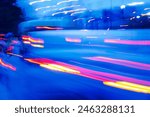 A blurry image of a busy street with cars and a bus. The image has a sense of motion and energy, as if it were captured in a time-lapse. The blue and red colors of the cars