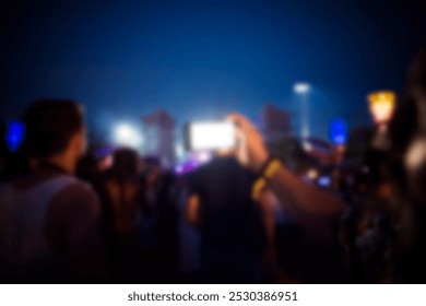 Blurry image of a crowd at a concert, with a focus on a smartphone capturing the event. Nighttime setting with colorful lights and people enjoying the music concert. Blurred concept scene. - Powered by Shutterstock