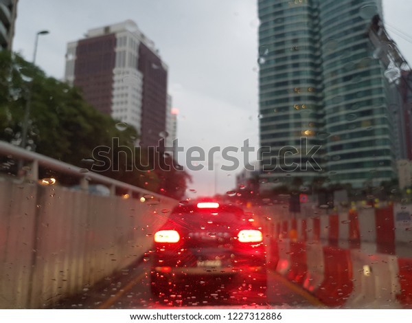 Blurry image due to\
rainwater wash on a windscreen while driving in a city during rush\
hours in the evening