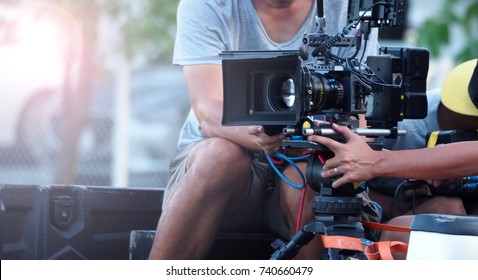 Blurry image of movie shooting or video production and film crew team with camera equipment at outdoor location and light flare effect. 