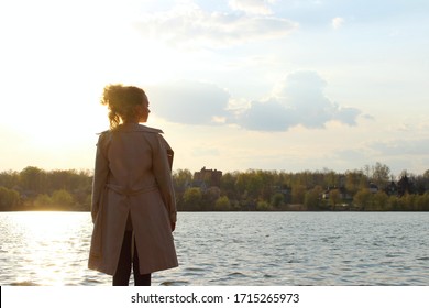 Blurry Image Of Teenage Girl Wearing A Beige Coat And Blue Jeans Standing Near The Water, Overexposed Shot.  People, Travel, Nature Concept.