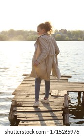 Blurry Image Of Teenage Girl Wearing A Beige Coat And Blue Jeans Standing Near The Water, Overexposed Shot.  People, Travel, Nature Concept.