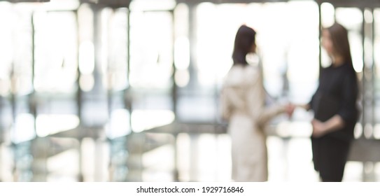 Blurry Image Of Two Business Women Meeting Each Other With A Handshake.