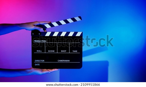 Blurry images of movie slate or clapper\
board. Hand holds empty film making clapperboard on color\
background in studio for film movie shooting or recording. Film\
slate for Youtuber video\
production.