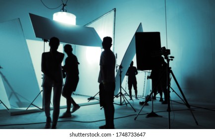 Blurry Images Of VDO Production Crew Team Working In Photo Shooting Studio Which Backdrop And LED Headlight Flash On Tripod And Professional Equipment For Video Online Filming