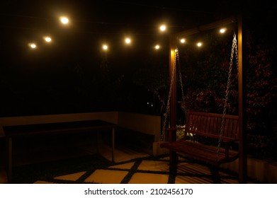 Blurry Light Bulb And Empty Swing In Backyard At Night 