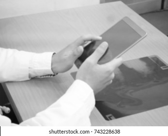 The Blurry Light Design Background Of Human In White Uniform,Doctor Is Working By Hold Ipad In Hand And X-ray Film Put On Table,in Black And White Tone,