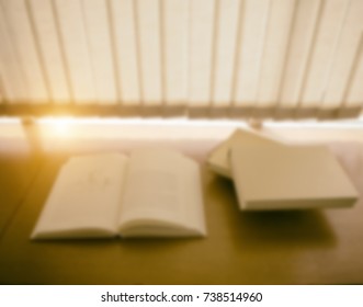 the blurry light design background of the opened book was put on wood desk near window,warm light tone,at library room