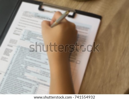The blurry liight design background of human hand with pen is signing on The Insurance Claim Form,on wooden desk,vintage tone.