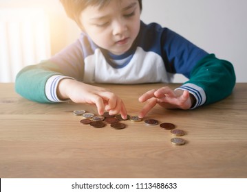 Blurry Little Boy Face Counting Pound Coins On Wooden Table, Kid Learning How Different About Money Coins, Children Learning  About Financial Responsibility Or Planning Savings Concept.