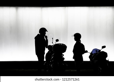 Blurry Natural Silhouettes  Of Man And Woman Putting Helmet And Preparing To Sit On A Motorbike In Front Of Modern Building  In The Night In Black And White