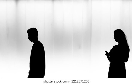 Blurry natural silhouettes of young woman looking at mobile and young man walking past, in the night