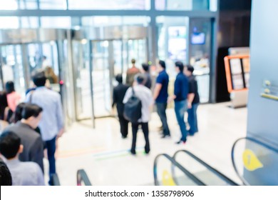 Blurry Of People Are Walking Out Of The Building Via A Rotating Glass Door.