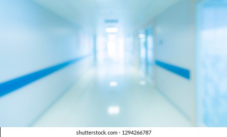 Blurry Photo Of Hospital Walk Way With Bright Clean Blue Lighting. White Floor With Cool Tone Color With Light Tunnel In The Middle Of Picture Use For Background Purpose.Medical And Insurance Concept.