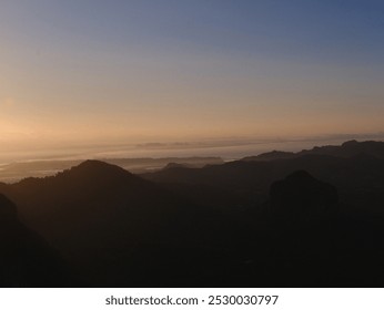 A blurry photo of a mountain range with a sunset in the background. The sky is a mix of orange and blue hues, creating a serene and peaceful atmosphere. The mountains are covered in shadows - Powered by Shutterstock