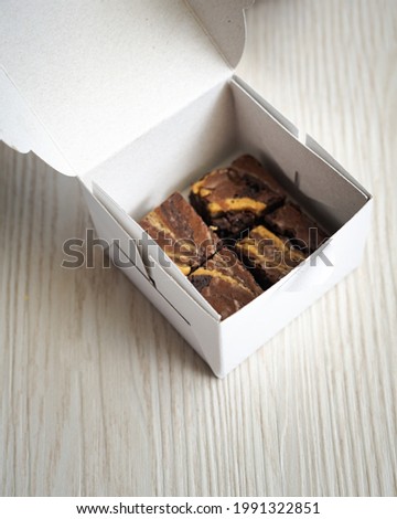 Blurry photo of a set of brownies in a takeaway paper box container.