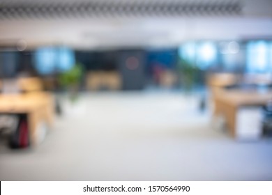 A Blurry Photograph Of An Office Setting. The Open Corridor Is Flooded With Natural Light From The Glass Wall On The Left. Blurred Office Interior Space Background