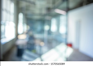 A Blurry Photograph Of An Office Setting. The Open Corridor Is Flooded With Natural Light From The Glass Wall On The Left. Blurred Office Interior Space Background