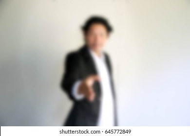 Blurry Portrait Of Businessman Giving Handshake On Gray Background
