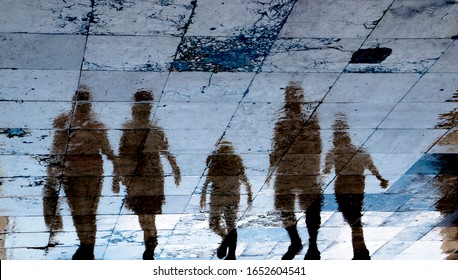 Blurry Reflection Shadow Silhouette On Wet City Sidewalk Of Mysterious People Walking Away The Night, Low Angle View