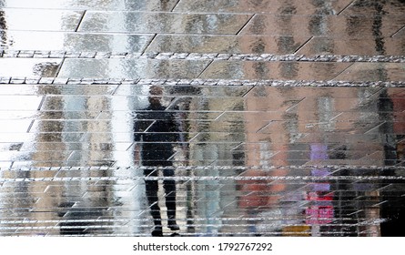 Blurry reflection shadow silhouette on wet puddle of a man walking a city street on a rainy day, abstract background
