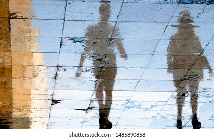 Blurry reflection shadow silhouettes of two people walking on a wet street  on a summer day in the city