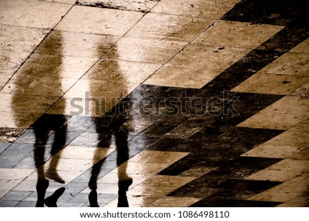 Blurry reflection shadow of two people walking the city street patterned sidewalk on a  rainy day