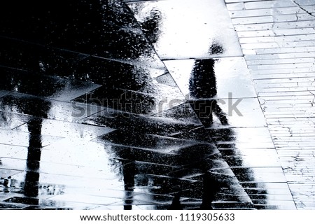 Blurry reflection  silhouette of one person  walking alone  on wet city park sidewalk on a rainy day