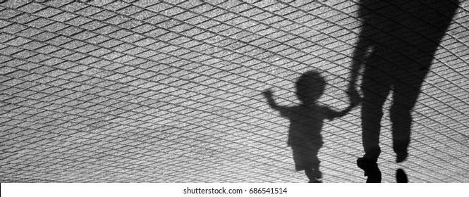 Blurry shadow of a joyful toddler boy and his father walking hand in hand on patterned sidewalk in black and white