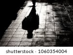 Blurry shadow and silhouette of a man standing in the night on wet city street sidewalk with water reflection in black and white