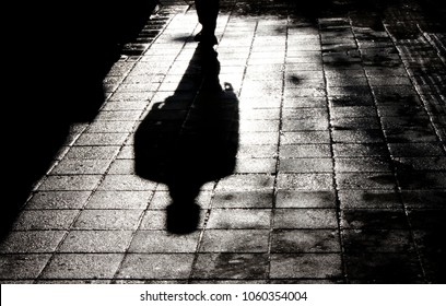 Blurry shadow and silhouette of a man standing in the night on wet city street sidewalk with water reflection in black and white