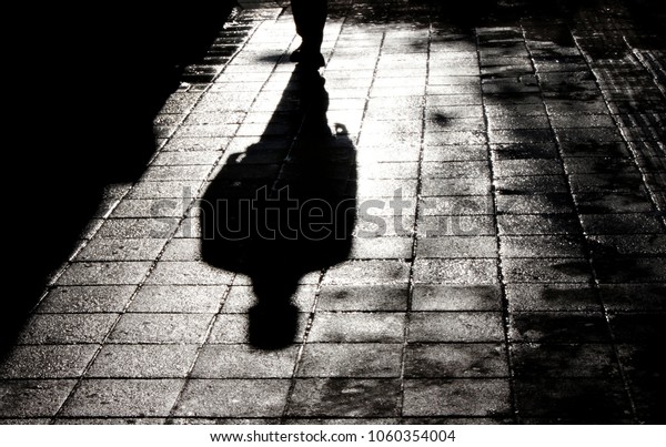 Blurry shadow and silhouette of a man standing in\
the night on wet city street sidewalk with water reflection in\
black and white