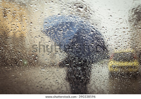 A blurry silhouette with umbrella on a city street\
seen through wet window