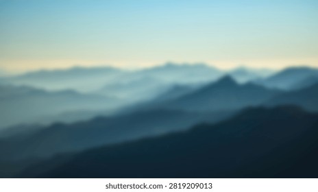 A blurry and soft focus view of layered mountain ridges covered in morning fog under a pale sky