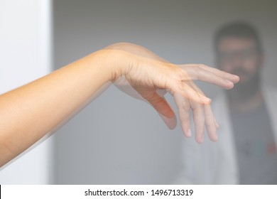 A blurry specialist neurologist physician is seen behind the shuddering hand of a caucasian person, unsteady tremors symptomatic of Parkinson's disease. - Shutterstock ID 1496713319