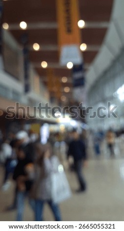 Blurry view of a large crowd at the Auto Show inside the convention hall, with vibrant lights and displays in the background, creating a lively and busy bokeh effect.