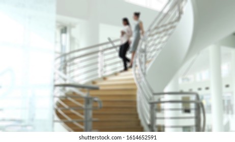 Blurry View Of Two Business Women Are Descending A Circular Staircase Leading To The Lobby Of An Big Office.