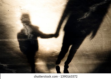 Blurry vintage shadow silhouettes of father and son walking hand in hand in old asphalt road  in sepia black and white 