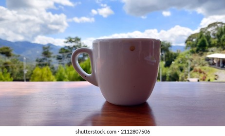 Blurry White Coffee Cup On Wooden Table, Side View Against Mountain View Background