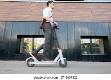 Blurry young businessman on scooter moving forwards along wall of contemporary business center while going home after work - Powered by Shutterstock