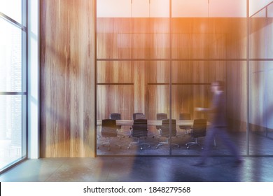 Blurry young businessman walking in modern meeting room with wooden walls, concrete floor and long conference table. Toned image