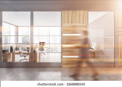 Blurry young businessman walking in modern office hall with gray and wooden walls and open space office in background. Toned image