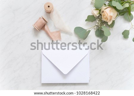 Blush wedding bouquet with roses, wedding envelopes and silk ribbons on marble background