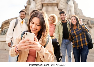 A Blushing And Embarrassed Woman Looks At The Phone While A Group Of Friends Wait In The Background. High Quality Photo