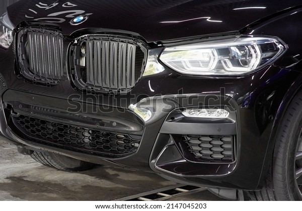 The BMW car, covered with a protective shiny black\
paint film, is in a repair shop. PPF polyurethane film protects car\
paint from stones and scratches, blurred focus. Chelyabinsk,\
Russia, May 07, 2021