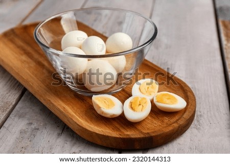 Board with bowl of boiled quail eggs on grey wooden background