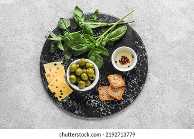 Board With Bowl Of Tasty Green Olives, Oil, Cheese, Crackers And Basil On Light Background