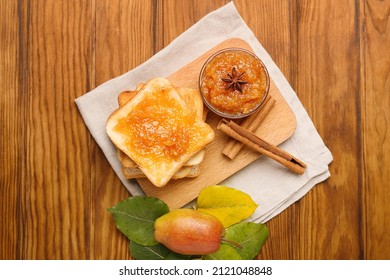Board with bowl of tasty pear jam and bread on wooden background