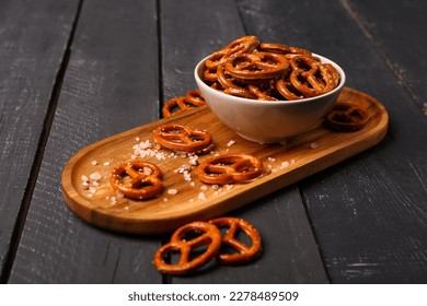 Board with bowl of tasty salted pretzels on dark wooden background - Powered by Shutterstock